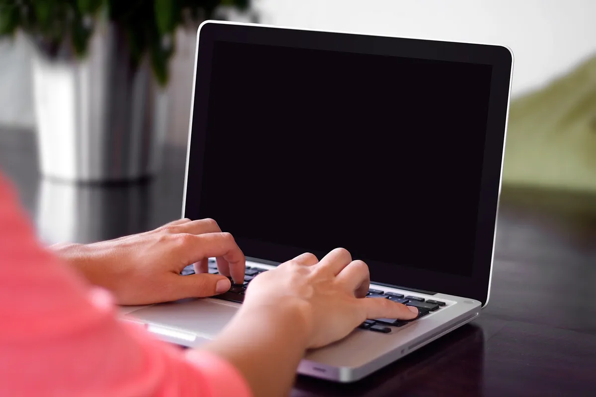 Dłonie piszące na klawiaturze laptopa przy jasnym blacie
